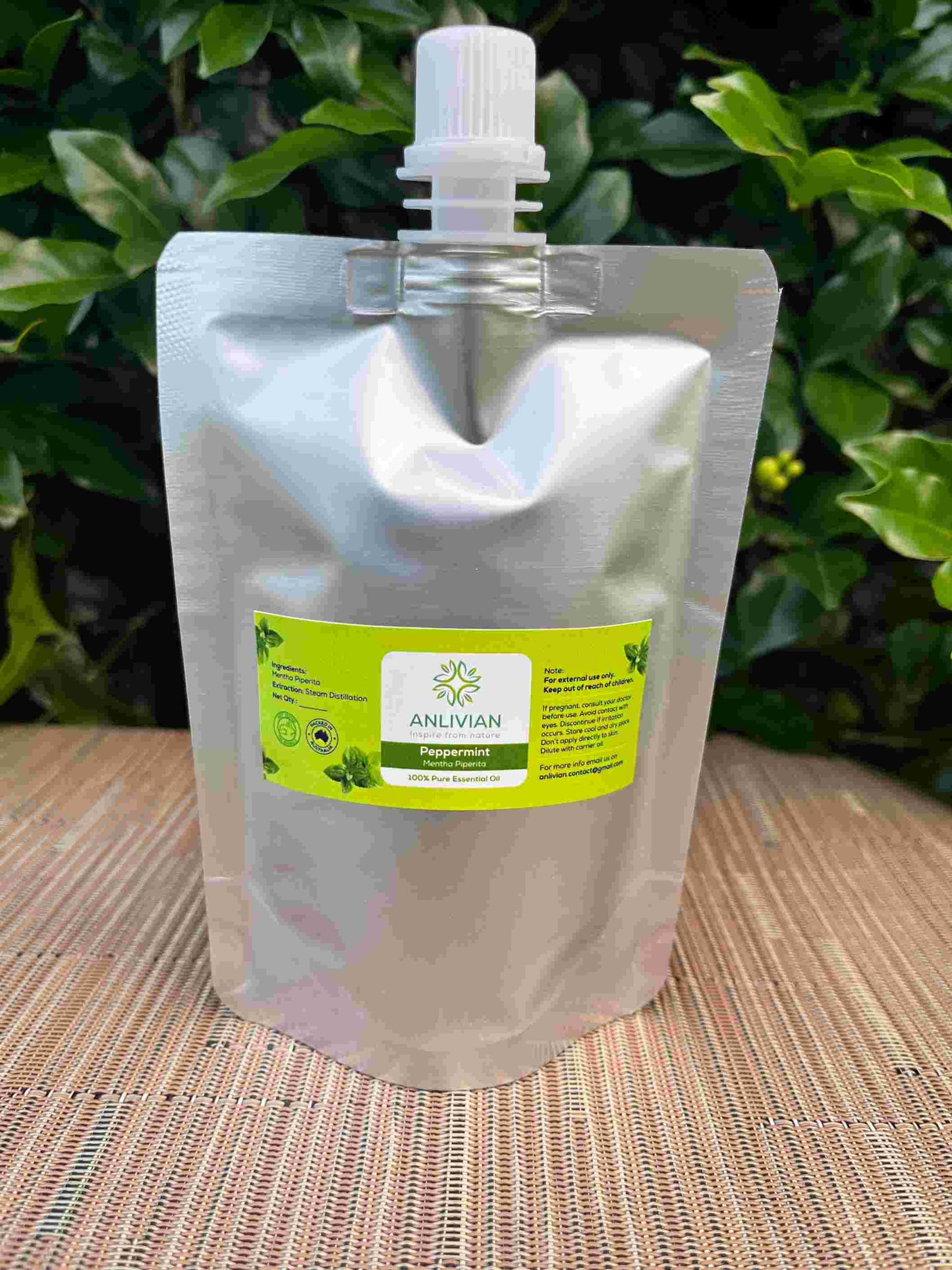 Silver foil pouch of Anlivian Peppermint Pure Essential Oil with a white spout cap, set against a background of green leaves and a woven surface.